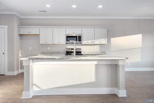 kitchen featuring crown molding, light wood-type flooring, appliances with stainless steel finishes, a kitchen island with sink, and white cabinets