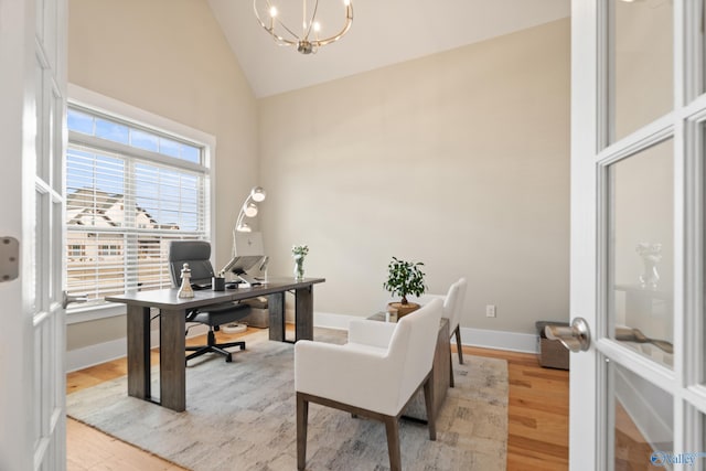 office space featuring light wood-type flooring, high vaulted ceiling, a notable chandelier, and baseboards