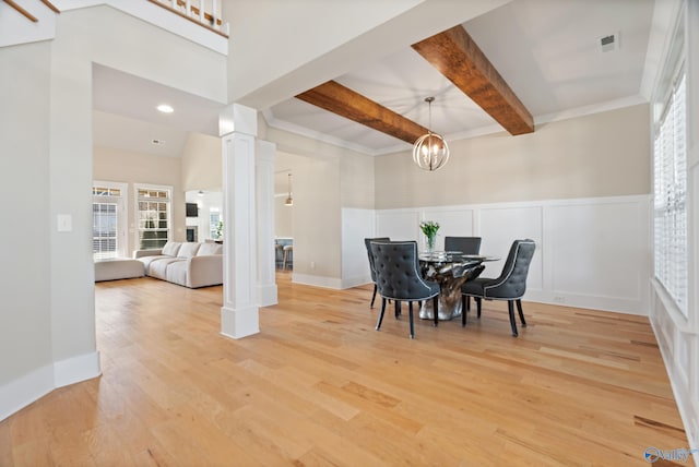 dining room with a decorative wall, decorative columns, beamed ceiling, light wood-type flooring, and wainscoting