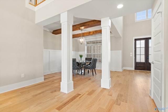 entryway with beam ceiling, light wood-type flooring, decorative columns, and wainscoting