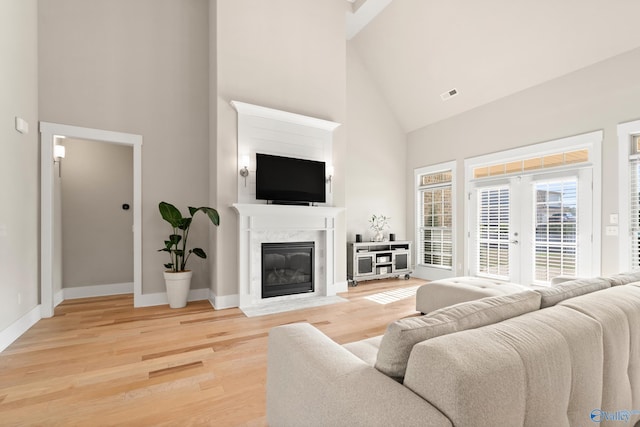 living area with visible vents, baseboards, a fireplace, light wood-style flooring, and high vaulted ceiling