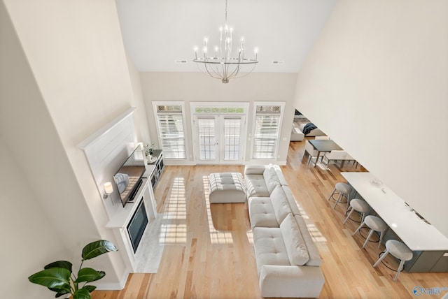 living area featuring an inviting chandelier, a high ceiling, visible vents, a high end fireplace, and light wood finished floors