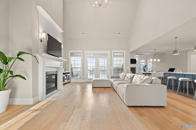living area featuring a glass covered fireplace, plenty of natural light, light wood-style floors, and an inviting chandelier