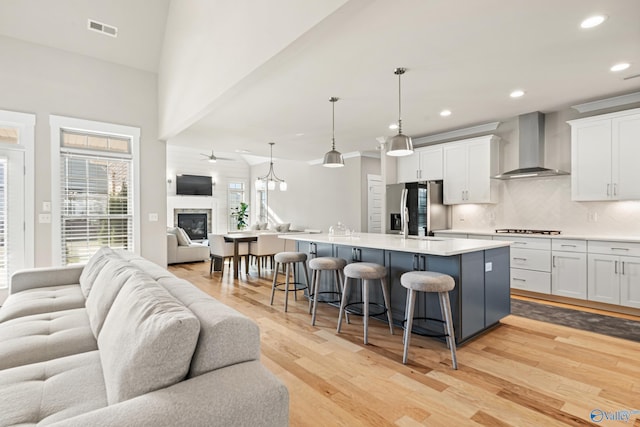 kitchen with stainless steel fridge with ice dispenser, visible vents, wall chimney exhaust hood, open floor plan, and cooktop