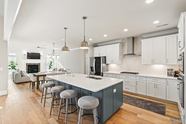 kitchen featuring wall chimney range hood, white cabinetry, a ceiling fan, visible vents, and appliances with stainless steel finishes
