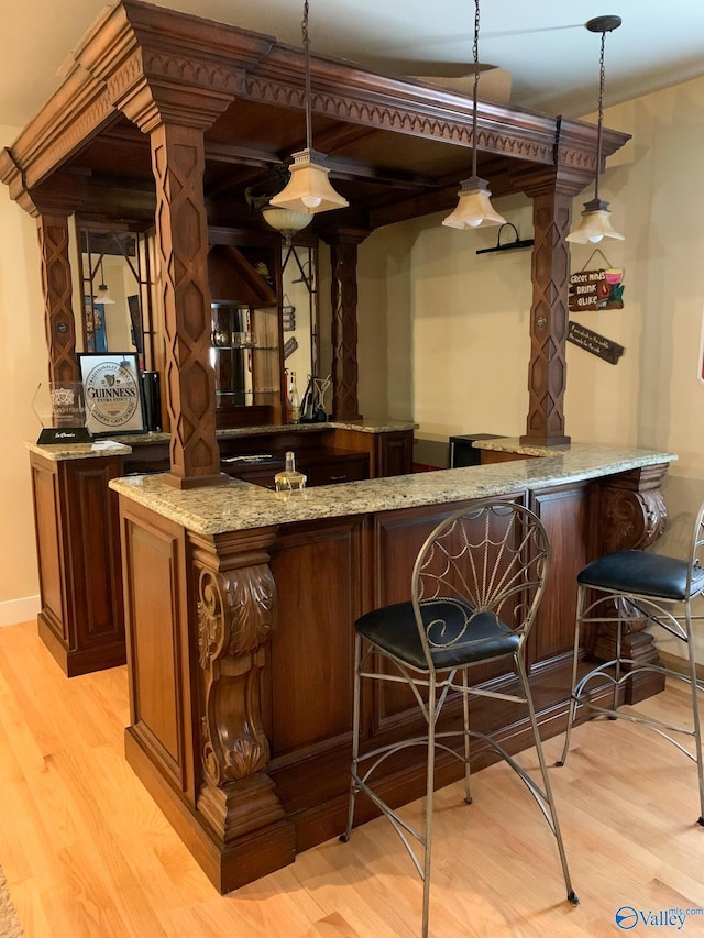 bar featuring light stone countertops, hanging light fixtures, and light hardwood / wood-style floors