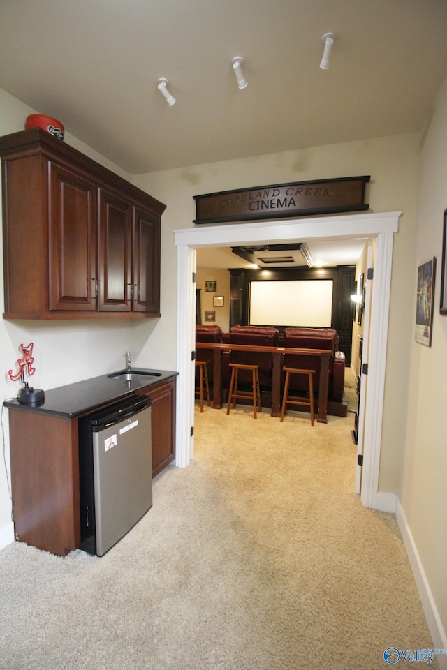 kitchen featuring dishwashing machine, light carpet, a sink, baseboards, and dark countertops