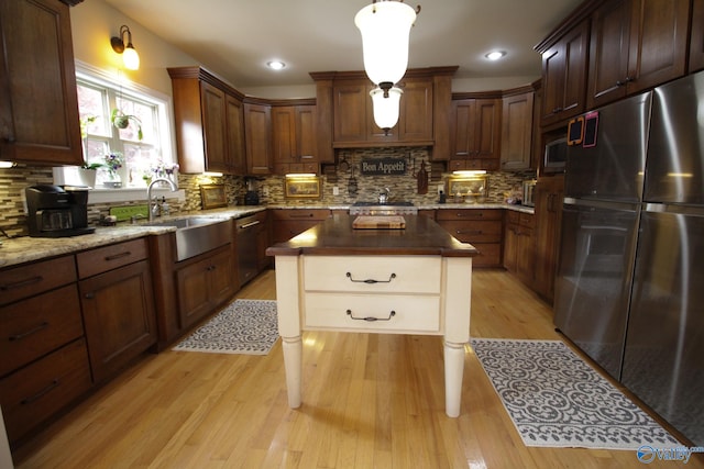 kitchen featuring light wood-type flooring, backsplash, stainless steel appliances, pendant lighting, and sink