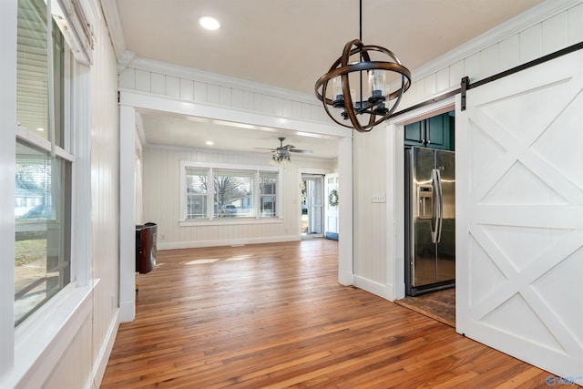 interior space with hardwood / wood-style flooring, ceiling fan, a barn door, and crown molding