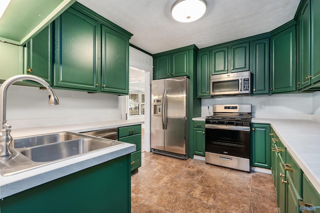 kitchen with a textured ceiling, stainless steel appliances, green cabinets, and sink