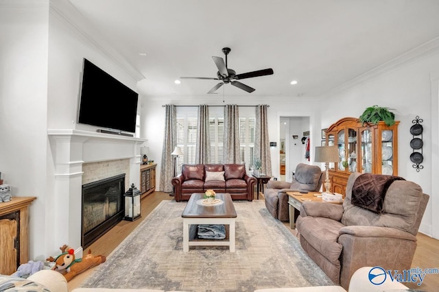 living room with crown molding, light wood-type flooring, recessed lighting, a tiled fireplace, and a ceiling fan