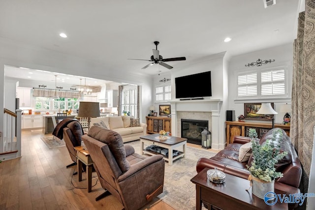 living room with recessed lighting, a fireplace with flush hearth, ceiling fan with notable chandelier, and light wood-style floors