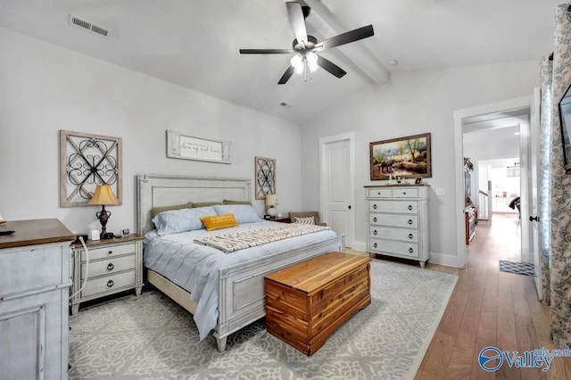 bedroom featuring a ceiling fan, visible vents, baseboards, vaulted ceiling with beams, and hardwood / wood-style floors