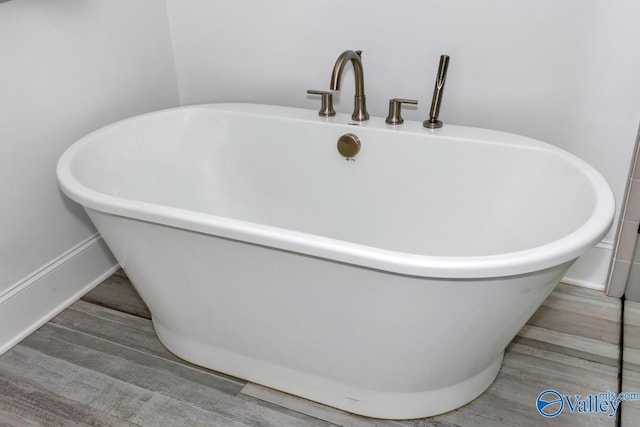 bathroom featuring a freestanding bath, baseboards, and wood finished floors