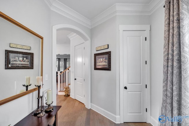 corridor with baseboards, ornamental molding, light wood finished floors, and arched walkways