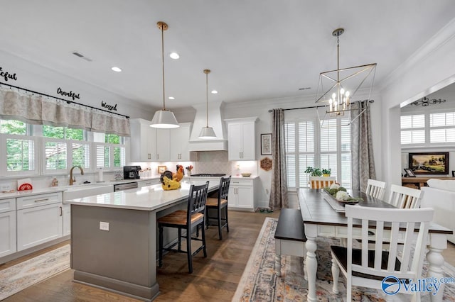 kitchen with a sink, a chandelier, a center island, decorative backsplash, and custom range hood