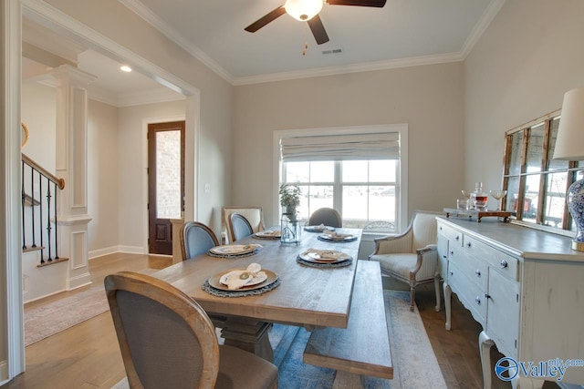 dining space featuring visible vents, stairs, light wood-type flooring, ornate columns, and crown molding