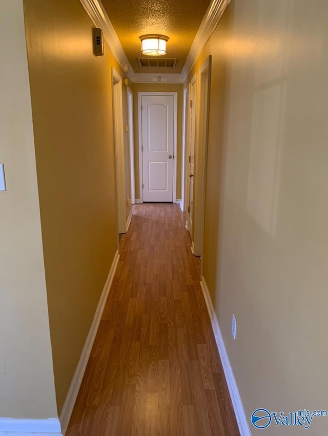 corridor featuring visible vents, a textured ceiling, baseboards, and wood finished floors