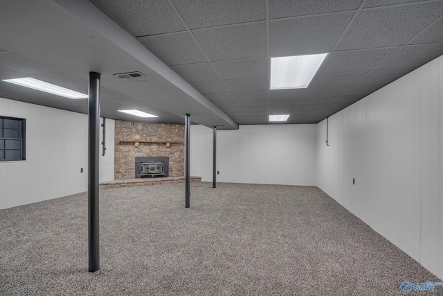 basement with carpet flooring, a wood stove, and a drop ceiling