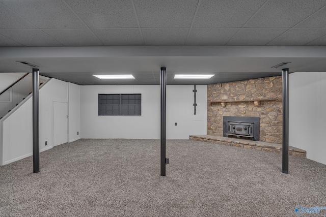 basement with a paneled ceiling, carpet floors, and a wood stove