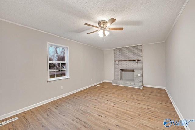 unfurnished living room featuring ceiling fan, a fireplace, light hardwood / wood-style floors, ornamental molding, and a textured ceiling