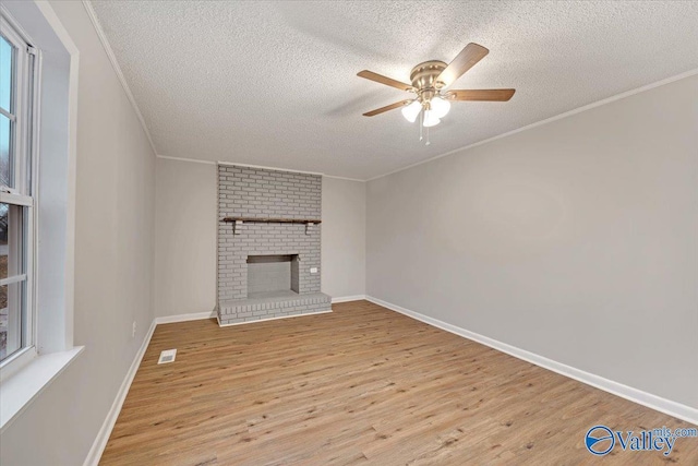 unfurnished living room featuring ceiling fan, light wood-type flooring, a fireplace, a textured ceiling, and ornamental molding