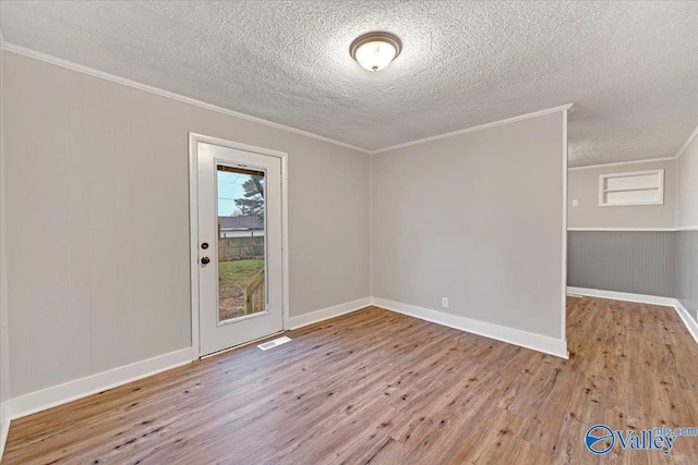 spare room with light wood-type flooring, crown molding, and a textured ceiling