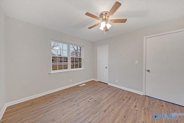 spare room featuring ceiling fan, light wood-type flooring, and a textured ceiling