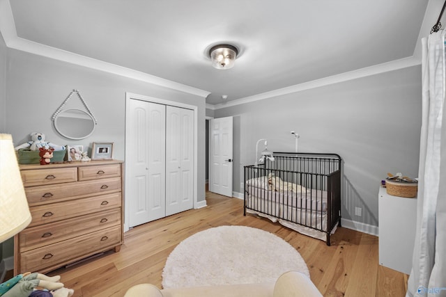 bedroom with ornamental molding, a nursery area, light hardwood / wood-style flooring, and a closet