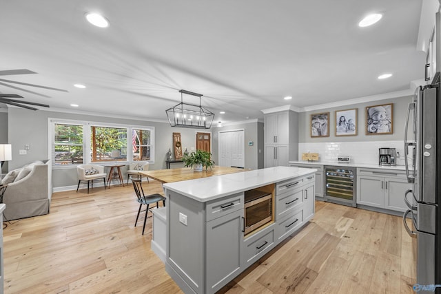 kitchen featuring a kitchen island, gray cabinetry, decorative light fixtures, beverage cooler, and appliances with stainless steel finishes