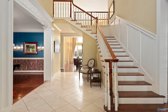 stairway featuring crown molding, light wood-type flooring, a chandelier, and ornate columns