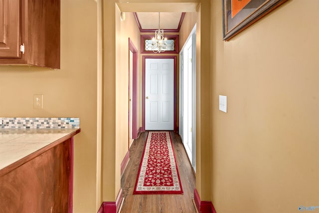 corridor with ornamental molding, a notable chandelier, and light wood-type flooring