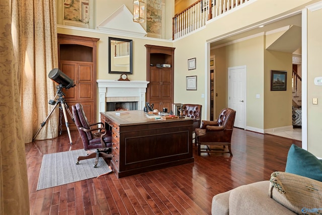 office space with crown molding, a tile fireplace, dark hardwood / wood-style flooring, and a high ceiling