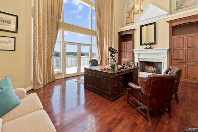 living room with a water view, a tile fireplace, dark hardwood / wood-style floors, and a towering ceiling