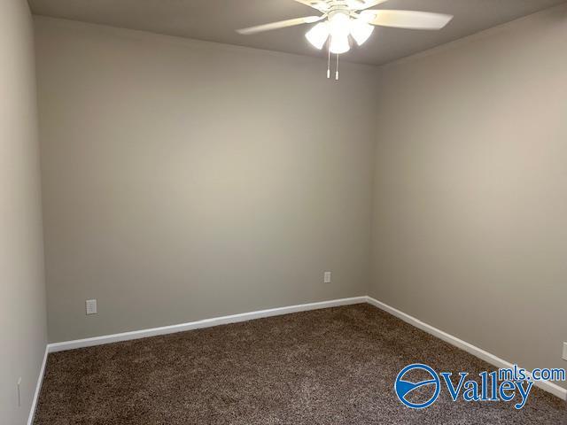 empty room featuring a ceiling fan, dark carpet, and baseboards