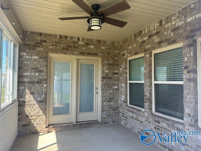 view of exterior entry with a ceiling fan, a patio area, and brick siding