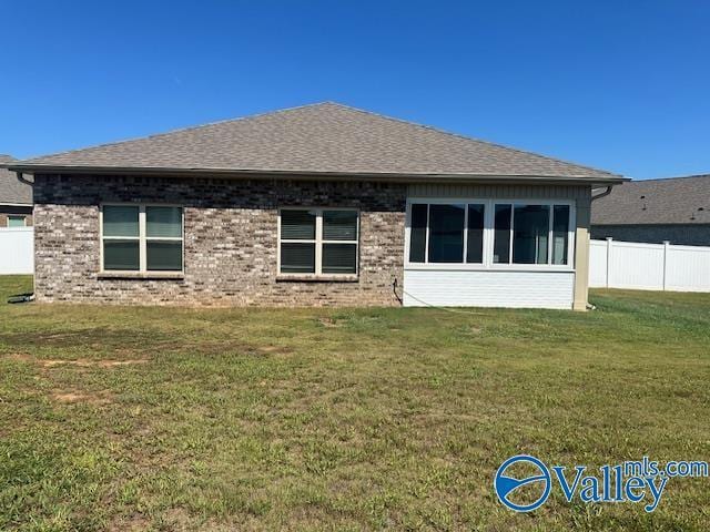 back of house with brick siding, roof with shingles, fence, and a yard