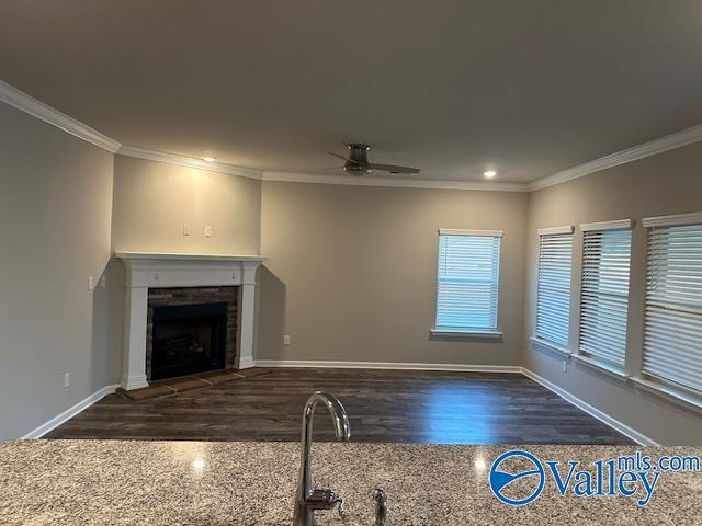 unfurnished living room featuring crown molding, a fireplace, a ceiling fan, wood finished floors, and baseboards