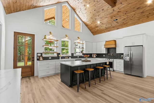 kitchen with appliances with stainless steel finishes, white cabinetry, high vaulted ceiling, a kitchen breakfast bar, and a center island