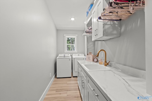 laundry area with cabinets, washer and dryer, sink, and light wood-type flooring