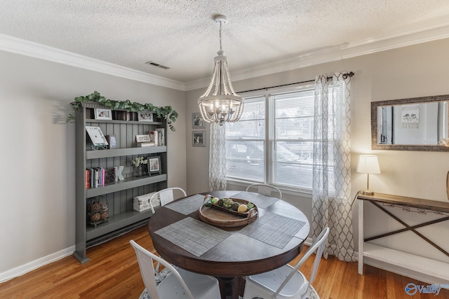 dining area featuring visible vents, an inviting chandelier, ornamental molding, a textured ceiling, and wood finished floors