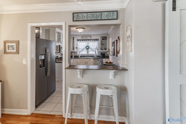 kitchen with dark countertops, ornamental molding, a kitchen breakfast bar, a peninsula, and black fridge