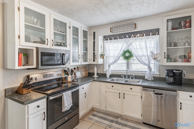 kitchen with dark countertops, appliances with stainless steel finishes, glass insert cabinets, white cabinetry, and a sink