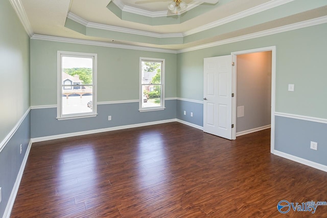 empty room featuring ornamental molding, dark wood-type flooring, ceiling fan, and a tray ceiling