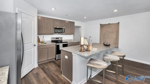 18882 Wicklow Cir, Athens, AL 35613 - kitchen with appliances with stainless steel finishes, dark wood-style flooring, a breakfast bar, light stone countertops, and baseboards