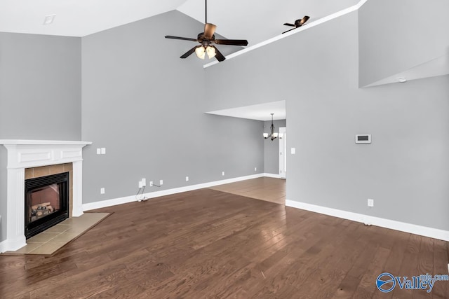 unfurnished living room featuring high vaulted ceiling, a tiled fireplace, ceiling fan with notable chandelier, and wood-type flooring