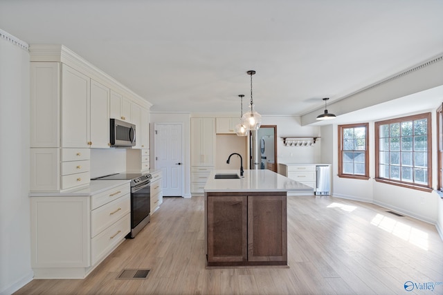 kitchen with white cabinets, appliances with stainless steel finishes, a kitchen island with sink, light wood-type flooring, and sink