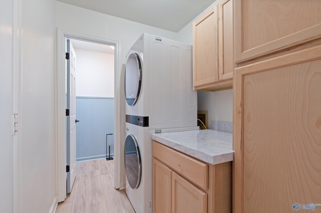 laundry area with stacked washer and clothes dryer, light wood-type flooring, and cabinets