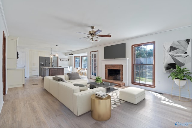 living room with crown molding, a brick fireplace, light wood-type flooring, and ceiling fan