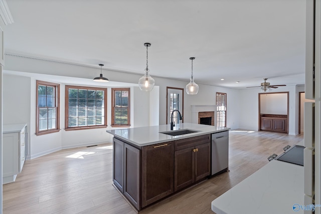 kitchen with an island with sink, light wood-type flooring, dishwasher, decorative light fixtures, and sink